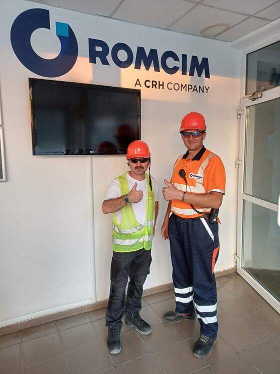 Coleg Compania DDD cu cască și vestă reflectorizantă, alături de un angajat Romcim, într-un punct de lucru al fabricii